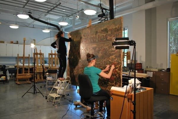 Two conservators examine a large artwork in a museum studio